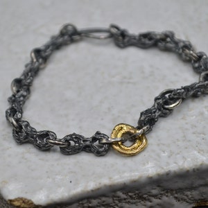 May include: A silver chain bracelet with a gold ring charm. The chain is made of small, textured links.