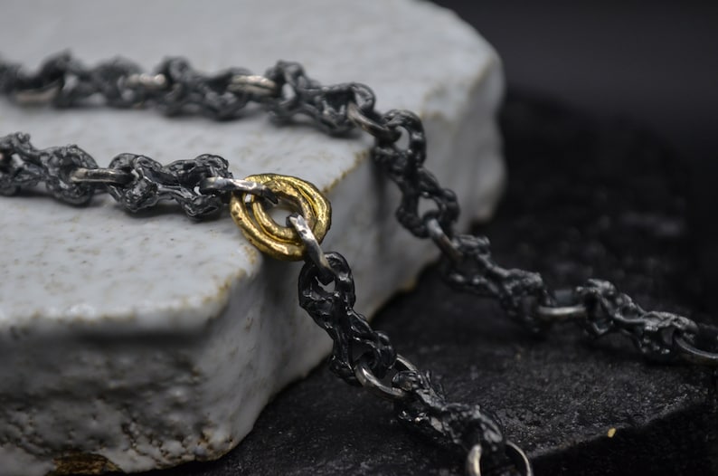 May include: A black oxidized silver chain necklace with a gold ring accent. The chain is made of small, textured links.