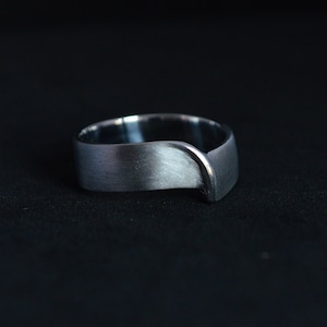 Könnte beinhalten: Ein silberner Ring mit einem einzigartigen, geschwungenen Design. Der Ring ist gebürstet und hat eine matte Oberfläche.