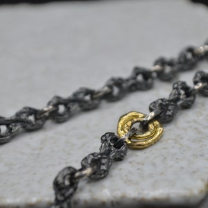 May include: A silver chain necklace with a gold ring accent. The chain is made of small, textured links.