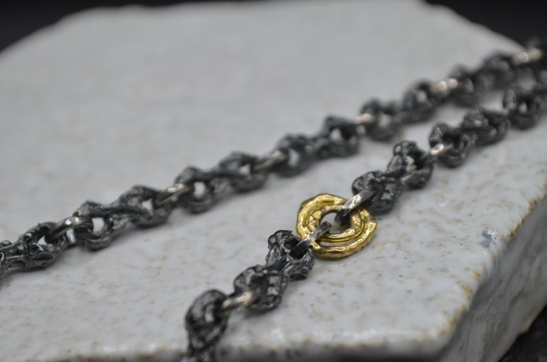 May include: A silver chain necklace with a gold ring accent. The chain is made of small, textured links.