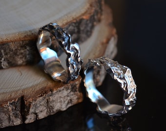 May include: Two silver rings with a textured, organic design. The rings are stacked on top of each other and are resting on a piece of wood.