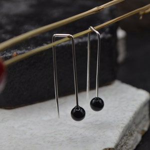 May include: A pair of silver dangle earrings with black round beads at the end.