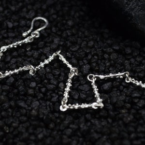 May include: Three silver chain bracelets with textured links. The bracelets are arranged in a triangular shape on a black background.