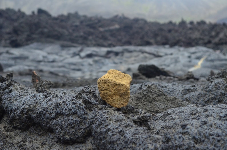May include: A single, rough, light brown rock sits on a bed of dark gray volcanic rock.