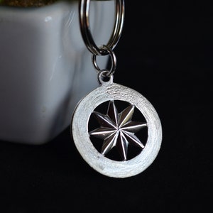 Puede incluir: Llavero de plata con un dije circular con un diseño de estrella.