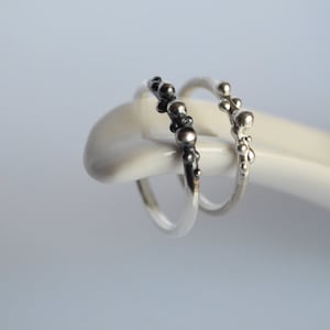 Könnte beinhalten: Zwei silberne Ringe mit einem Perlenmuster. Ein Ring hat schwarze Perlen und der andere hat silberne Perlen.