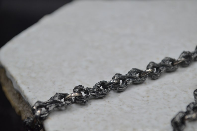 May include: A close-up of a silver chain necklace with a textured, organic design. The chain is made of small, interconnected links that resemble branches or vines.
