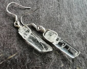 Puede incluir: Un par de pendientes de plata con colgantes de cristal de cuarzo transparente. Los cristales son largos y delgados, con un aspecto natural y en bruto. Los pendientes son simples y elegantes, perfectos para el uso diario.