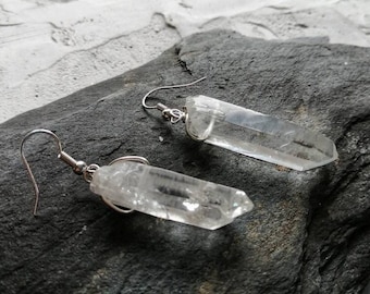 May include: A pair of silver earrings with clear quartz crystal points. The crystals are long and slender, and they are suspended from the earrings by a simple wire loop.