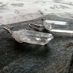 Puede incluir: Un par de pendientes de plata con colgantes de cristal de cuarzo transparente. Los cristales son facetados y tienen un aspecto natural y en bruto.