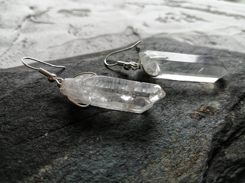 Puede incluir: Un par de pendientes de plata con colgantes de cristal de cuarzo transparente. Los cristales son facetados y tienen un aspecto natural y en bruto.