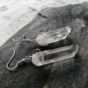 Puede incluir: Un par de pendientes de plata con colgantes de cristal de cuarzo transparente. Los cristales son largos y delgados, con una punta puntiaguda.
