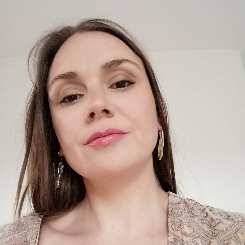 Puede incluir: Una mujer con el pelo largo y casta&ntilde;o lleva una blusa de lentejuelas marr&oacute;n claro y pendientes de oro. Mira a la c&aacute;mara con una expresi&oacute;n neutral.