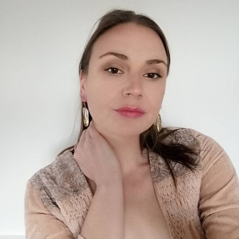 Puede incluir: Una mujer con el pelo largo y casta&ntilde;o lleva un c&aacute;rdigan marr&oacute;n claro con un delicado patr&oacute;n. Lleva pendientes de oro con una piedra transparente.