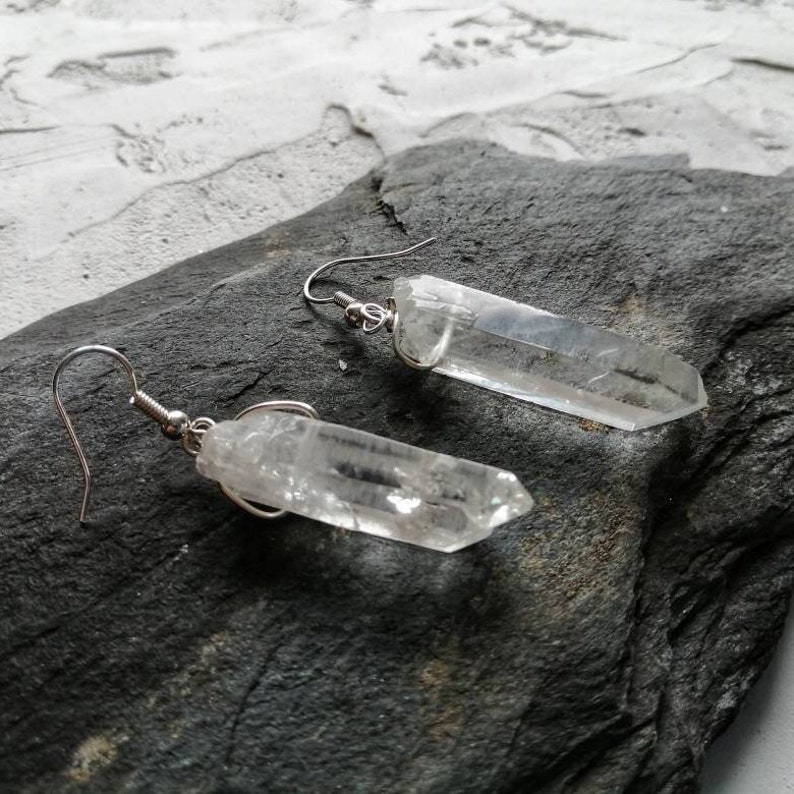 Puede incluir: Un par de pendientes de plata con puntas de cristal de cuarzo transparente. Los cristales son largos y delgados, y est&aacute;n suspendidos de los pendientes mediante un simple bucle de alambre.