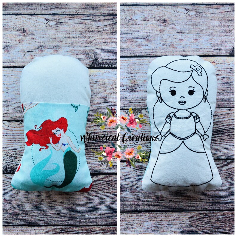 May include: A white pillow with a black outline of a princess on one side and a colorful print of a mermaid on the other side.