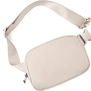 May include: A beige fanny pack with an adjustable strap and a plastic buckle closure. The pack has a rectangular shape with a zippered main compartment. The strap is made of a matching beige material.