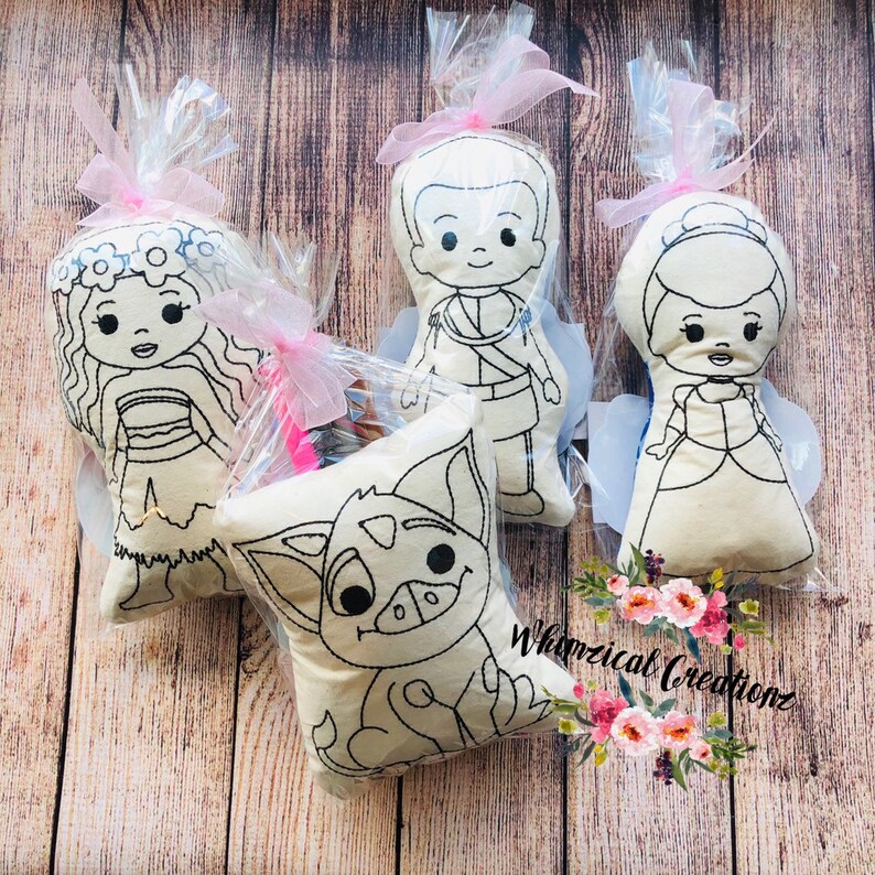 May include: Four color-your-own plush toys in individual clear plastic bags with pink ribbon. The toys are a princess, a prince, a girl with a flower crown, and a cartoon animal. Whimsical Creations is printed on the bottom right corner of the image.