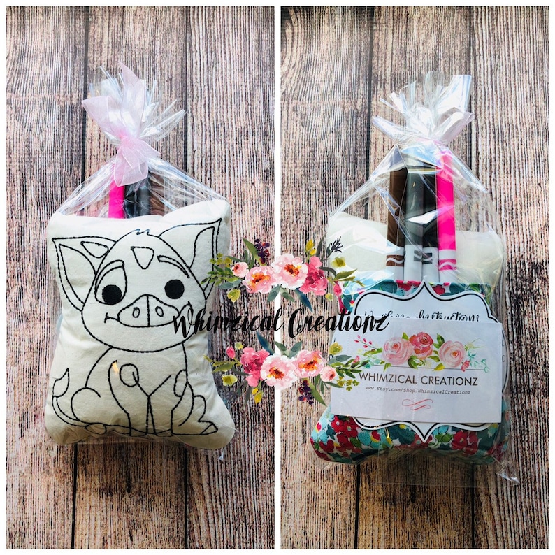 May include: A white pillow with a black outline of a cartoon pig. The pillow is packaged in a clear plastic bag with pink ribbon. The bag also contains markers for coloring the pig.