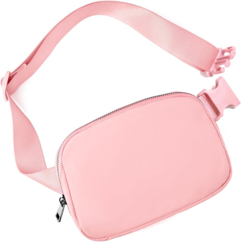 May include: A light pink fanny pack with a matching adjustable strap and buckle closure. The bag features a zippered main compartment and a sleek, minimalist design. The strap is approximately 40 inches long.