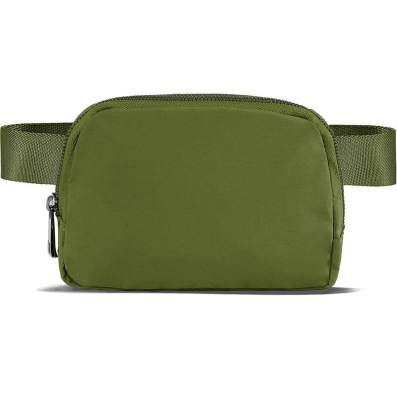 May include: Olive green fanny pack with a zippered main compartment and adjustable strap. The bag has a minimalist design and a silver-colored zipper pull. The strap is the same color as the bag.