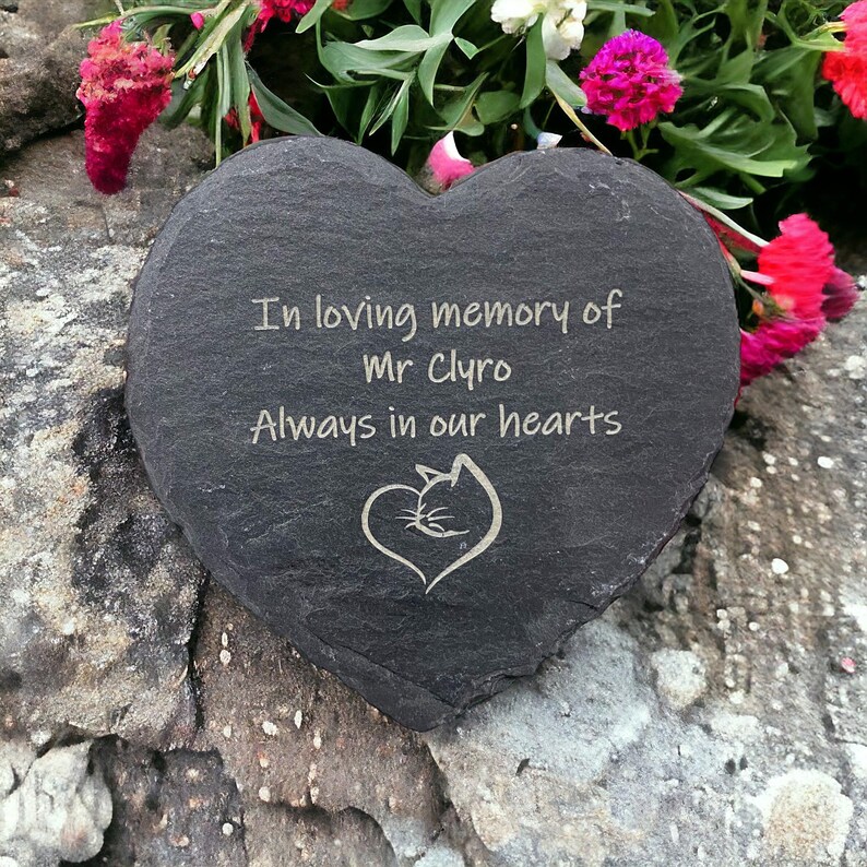 May include: A black heart-shaped slate stone with the inscription "In loving memory of Mr. Clyro Always in our hearts" and a small engraved image of a cat inside a heart.