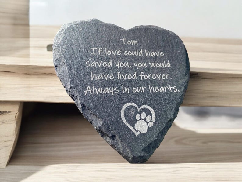 May include: A gray heart-shaped slate stone with the inscription "Tom If love could have saved you, you would have lived forever. Always in our hearts." and a paw print inside a heart.