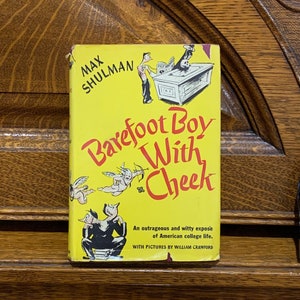 May include: A vintage paperback book titled "Barefoot Boy With Cheek" by Max Shulman. The cover is yellow with red and black text and illustrations. The book promises an outrageous and witty expose of American college life.