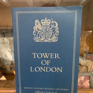 May include: A blue guidebook for the Tower of London, featuring the royal coat of arms and the text "Tower of London" and "Ministry of Public Building and Works".