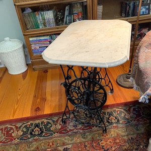 May include: A white marble top table with a black cast iron base. The table is on a rug with a red, blue, and gold pattern.