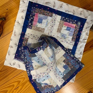 May include: Two blue and white patchwork quilt squares with a floral pattern. The squares are made of different fabrics and are sewn together to create a unique design.