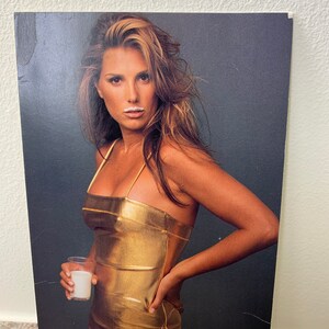 May include: A woman wearing a gold metallic dress holds a glass of milk. She has a white milk mustache.