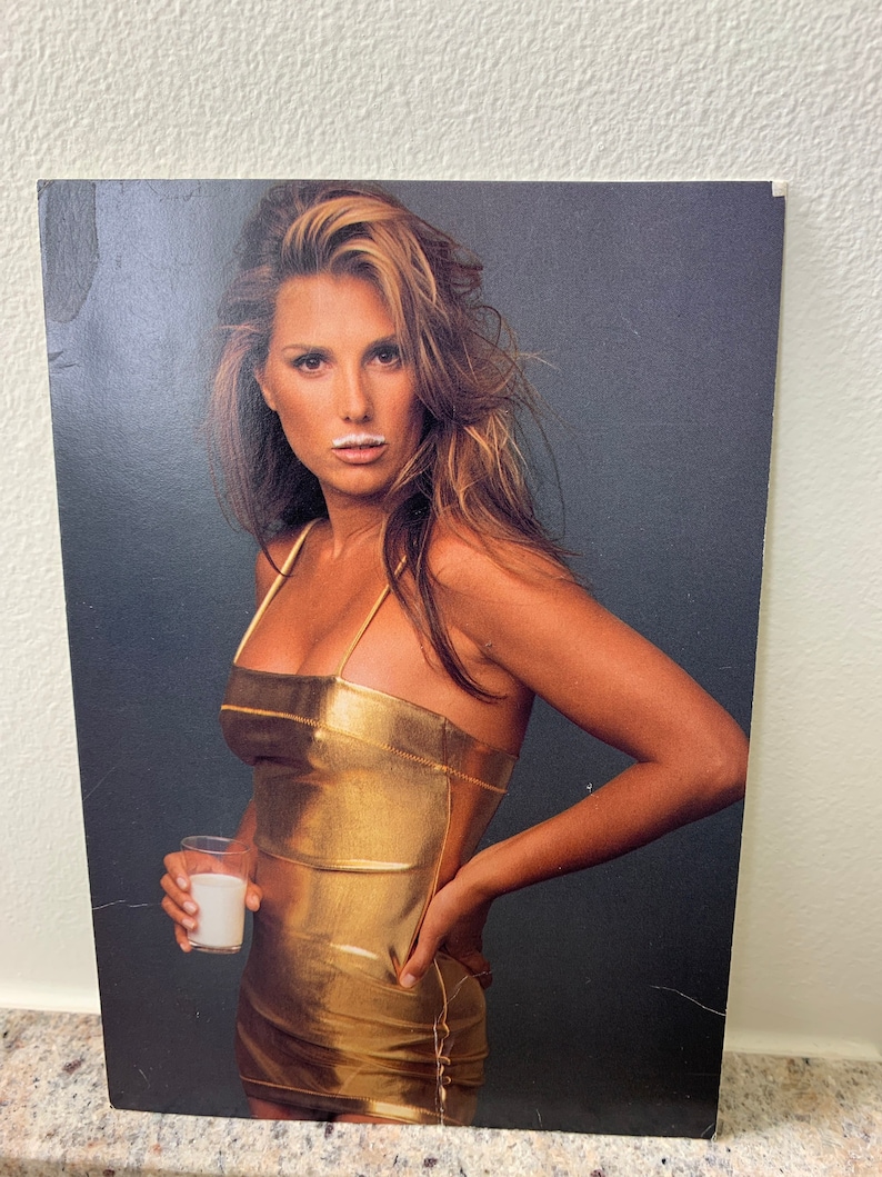 May include: A woman wearing a gold metallic dress holds a glass of milk. She has a white milk mustache.