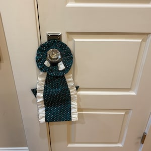 May include: A green and white doorstop with a white ruffle trim and a small white ghost design. The doorstop is hanging on a white door knob.