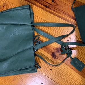 Puede incluir: Un conjunto de bolso tote y bandolera verde oscuro. El bolso tote tiene asas largas y un compartimento principal grande. El bolso bandolera tiene una correa para el hombro y forma rectangular. Ambos bolsos tienen un aspecto texturizado y una etiqueta que dice "for people".