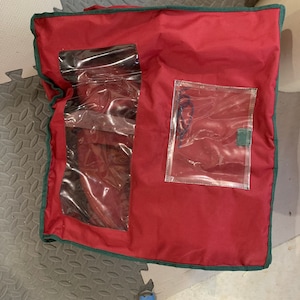 May include: Red storage bag with green trim and two clear plastic windows. The bag has a zipper closure.