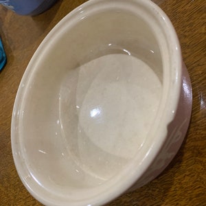May include: A white ceramic bowl with a pink rim. The bowl is empty and has a slight sheen.