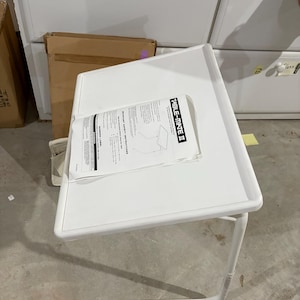 May include: White Table-Mate II lap desk with a white frame and a rectangular tabletop. The tabletop has a raised edge and a document is placed on top. The desk is designed to be used while sitting.