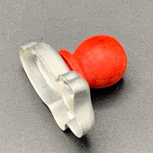 May include: A silver metal cookie cutter shaped like a Christmas tree with a red plastic handle.
