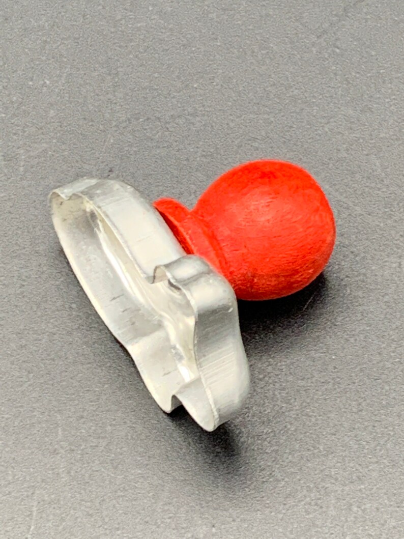May include: A silver metal cookie cutter shaped like a Christmas tree with a red plastic handle.