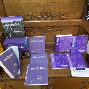May include: A collection of purple and white Aldus PageMaker manuals and guides, including a user manual, getting started guide, commercial printing guide, and Aldus additions. The manuals are on a wooden surface.