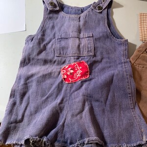 May include: A pair of blue denim overalls with a red bandana patch on the front. The overalls have frayed edges and are in a worn condition.