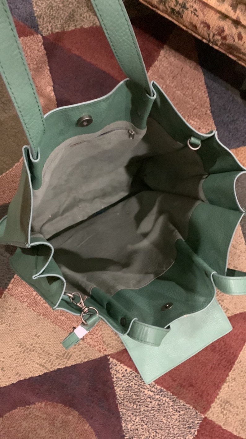 Puede incluir: Vista abierta de un bolso tote de cuero verde con una bolsa desmontable a juego. El bolso tiene dos asas y un cierre magn&eacute;tico a presi&oacute;n. El interior es de un tono verde m&aacute;s claro.