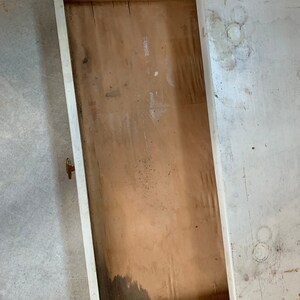 May include: A white painted wooden drawer with a brown wooden interior. The drawer is open and the interior is visible. The drawer is slightly dirty and has some wear and tear.