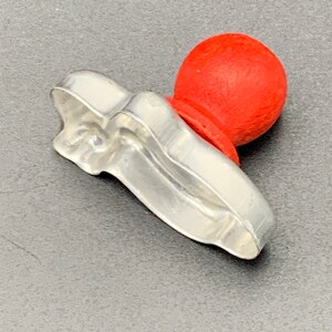 May include: A silver cookie cutter shaped like a shoe with a red plastic knob on top.