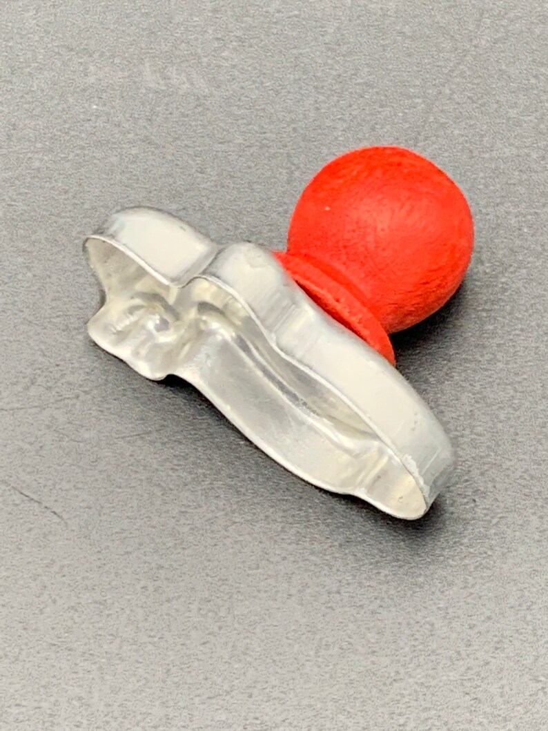 May include: A silver cookie cutter shaped like a shoe with a red plastic knob on top.