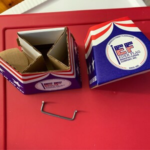 May include: Two blue and red cardboard boxes with the text "America's Finest Flagmakers" and "Eder Flag Manufacturing Company, Inc. Since 1903" on the front. A silver metal handle is also pictured.