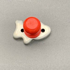 May include: A silver metal cookie cutter shaped like a fish with a red plastic top.