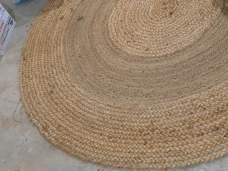 May include: A round, natural fiber rug with a woven texture. The rug is made of jute and has a light brown color.
